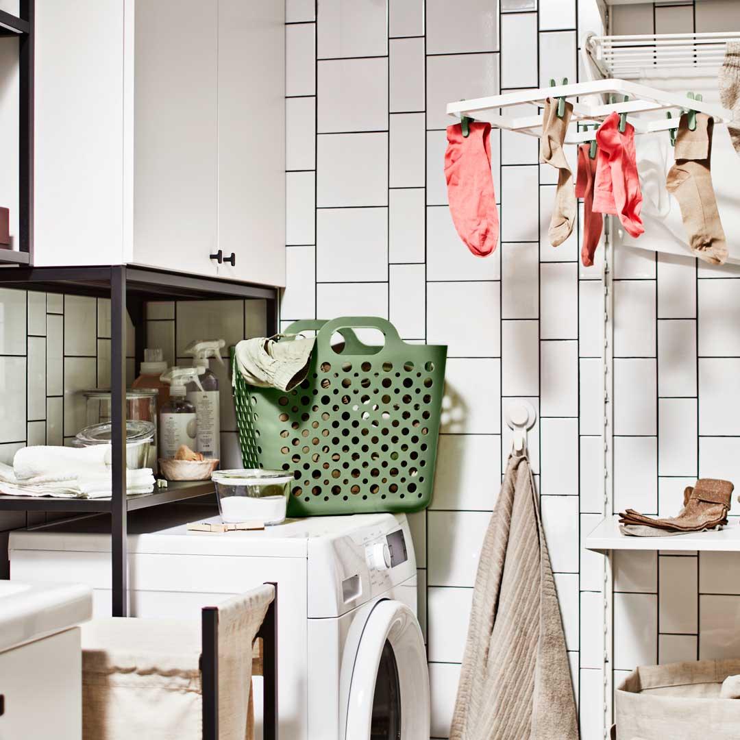 Pyykinpesukone, jonka päällä on ENHET-runko ja -seinäkaappi, sekä vihreä SLIBB-pyykkikori.