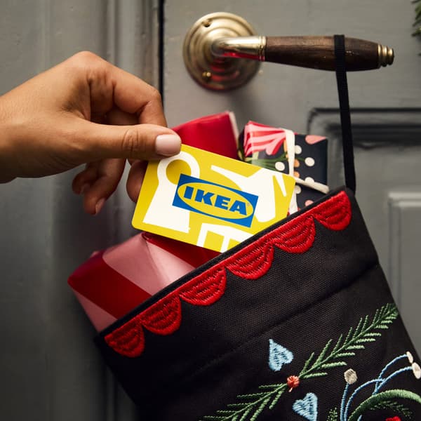 Qualcuno sta mettendo una carta regalo IKEA in un calzino natalizio appeso alla porta.