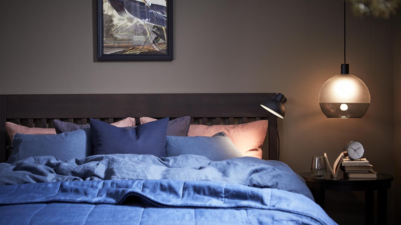 Quarto com luz ambiente com uma estrutura de cama IDANÄS e uma capa de edredão e fronhas PUDERVIVA em azul escuro.