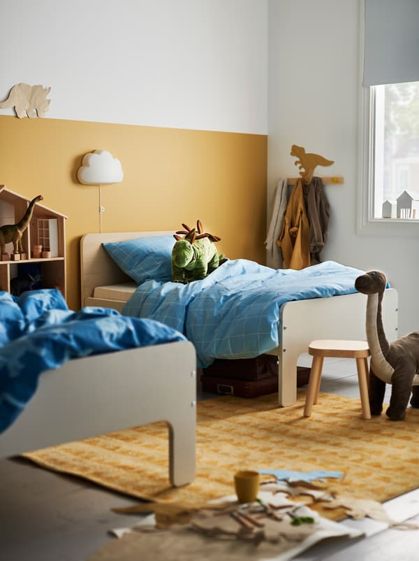 Quarto de criança com duas camas extensíveis SLÄKT de comprimentos diferentes, afastadas alguns metros, entre brinquedos e arrumação.