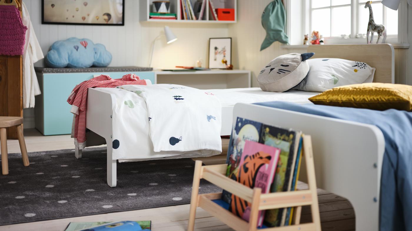 Quarto de criança com duas camas extensíveis SLÄKT em branco, lado a lado. Há brinquedos, decoração e arrumação no quarto.