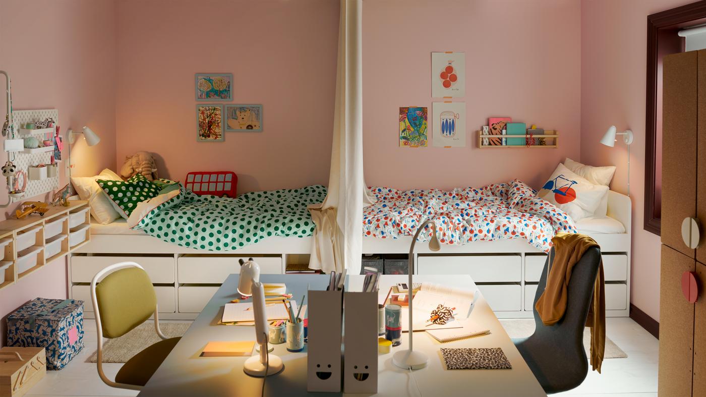 Quarto de criança partilhado, dividido em dois, com as camas voltadas uma para a outra e, em primeiro plano, duas secretárias voltadas uma para a outra.