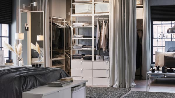Quarto em branco e cinzento com um roupeiro aberto, cortinados em cinzento claro e tapetes em cinzento escuro.