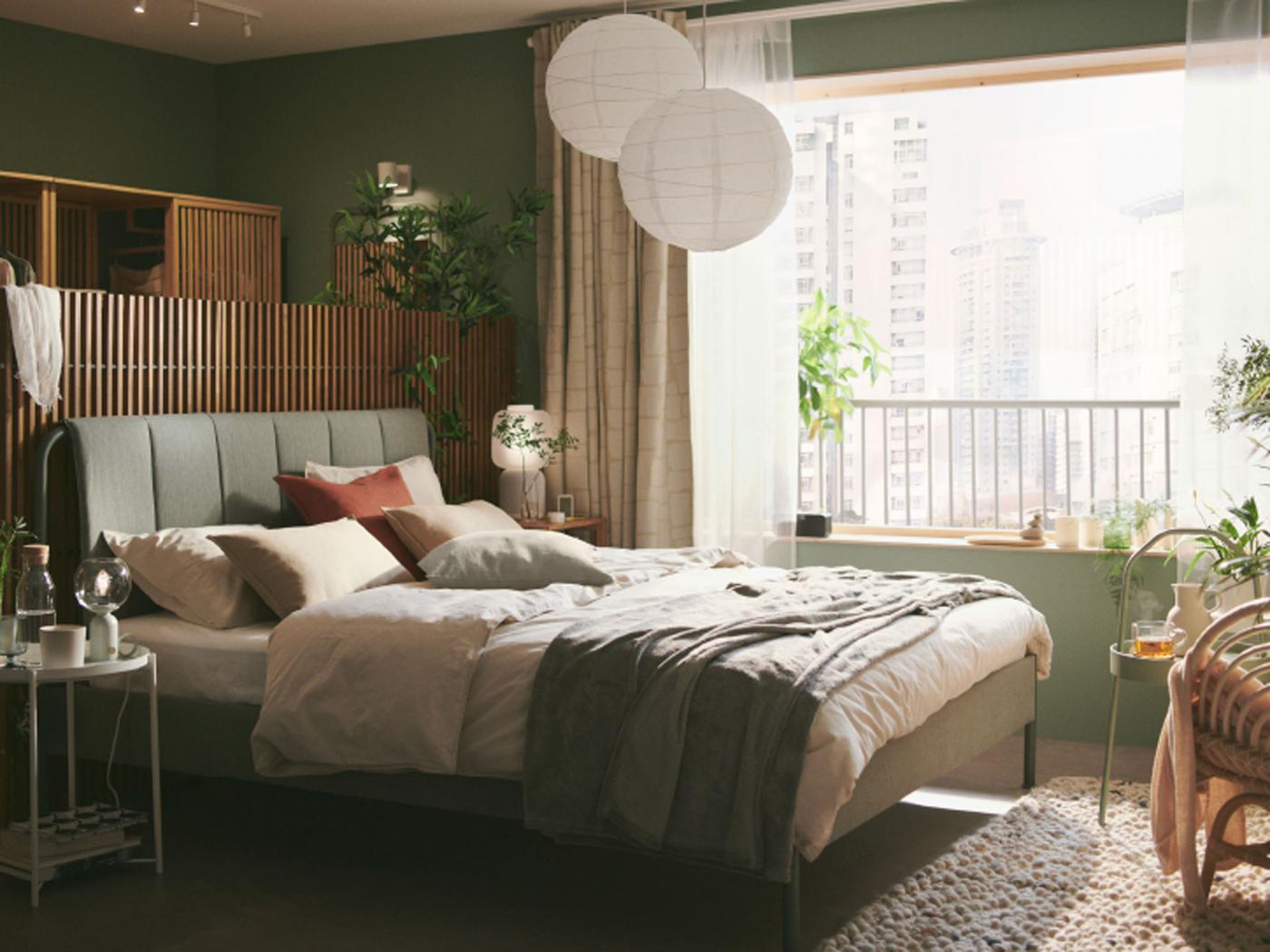 Quarto em verde suave com cama com roupa de cama ÄNGSLILJA em bege-cinzento claro, e dois candeeiros suspensos REGOLIT/HEMMA por cima.