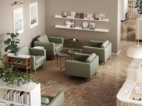 Quatre butaques LANDSKRONA verdes amb taules-safata GLADOM entre elles. Un prestatge per a quadres MOSLANDA amb revistes desades a la paret.