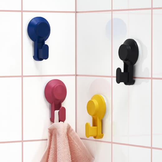 Quatre crochets de couleur vive collés aux murs carrelés avec une serviette suspendue à un crochet rouge.
