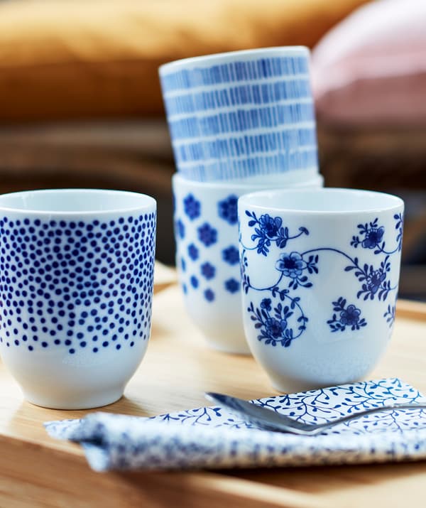 Quatre petites tasses blanches décorées avec différents motifs peints en bleu foncé.