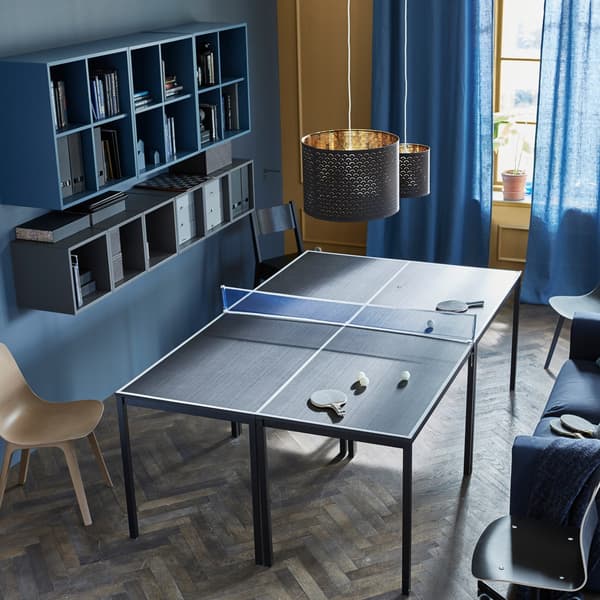 Quatre taules juntes per crear una taula de ping-pong, amb xarxa i raquetes.
