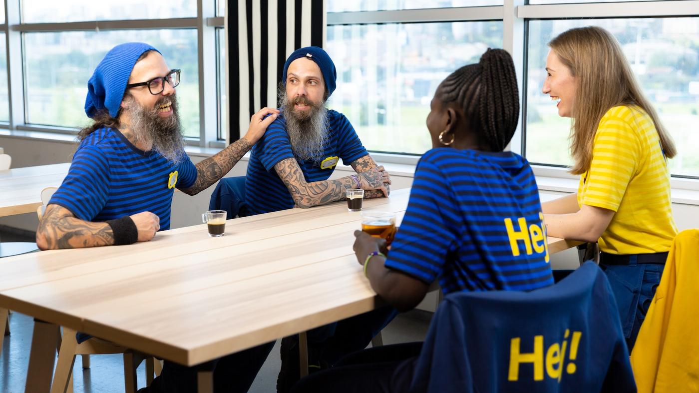 Quatres collaborateurs IKEA, deux hommes et deux femmes, en tenues de travail discutant autour d'une table rectangulaire