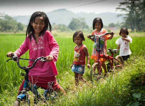 Quattro bambini in campagna che giocano e vanno in bici.