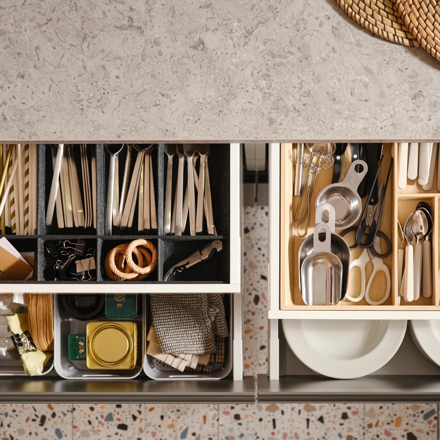Quattro cassetti della cucina MAXIMERA aperti con vari oggetti in un portaposate, un portatutto regolabile per cassetto e contenitori - IKEA.