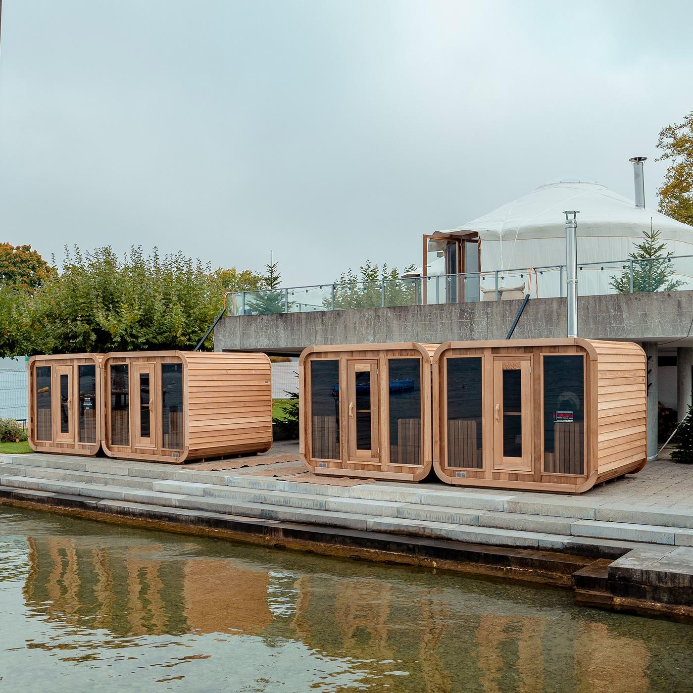 Quattro cubi di legno con dentro una sauna ciascuno lungo il bordo di una piscina