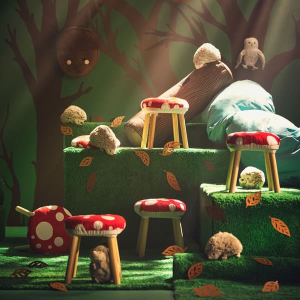 Quattro sgabelli colorati come dei funghi sono  illuminati dall'alto con dietro uno sfondo alberato. 