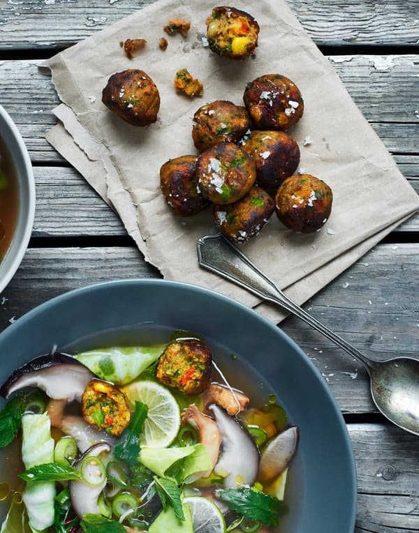 Quelques boulettes de légumes frites à côté d'un bol de soupe rempli de légumes, accompagnés de boulettes de légumes.