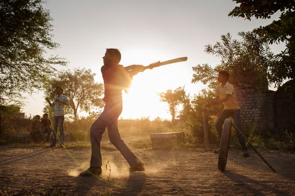 Quelques garçons qui jouent au cricket sur un terrain en terre battue au coucher de soleil.