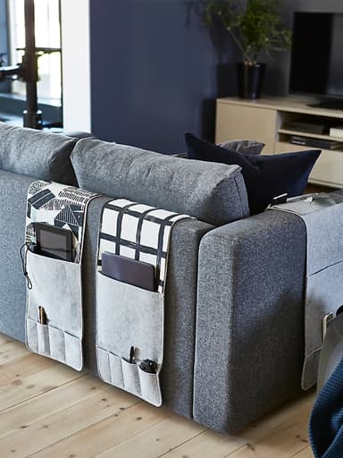 Queres un organizador para o sofá? KNALLBÅGE de IKEA é un organizador colgante de feltro gris para os accesorios, con petos para mandos a distancia, revistas e moito máis. Podes colgalo dos repousabrazos ou respaldos do sofá.