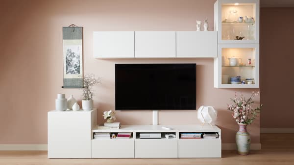 Rack TV BESTÅ blanco con una televisión y decoración en un living con pared rosada y piso de madera.