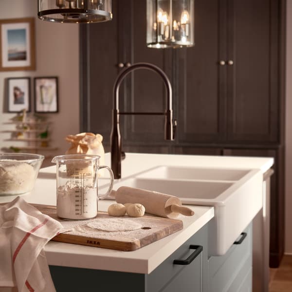 Radna ploča s imitacijom belog mermera, crna kombinovana slavina, tamnosivi frontovi fioka i drvena daska za seckanje s brašnom i testom.