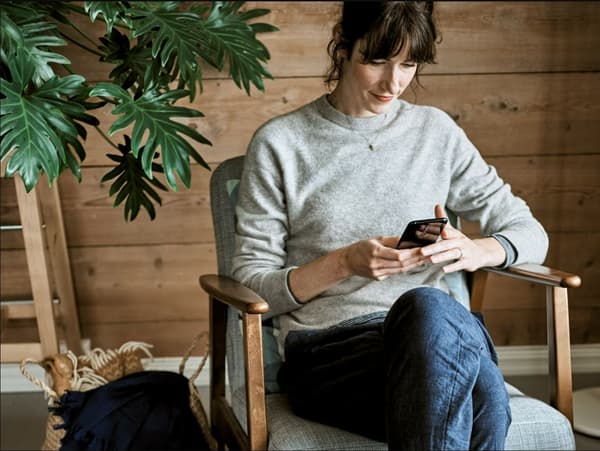 Ragazza seduta che guarda il sito web di IKEA su uno smartphone. Accanto una pianta verde.