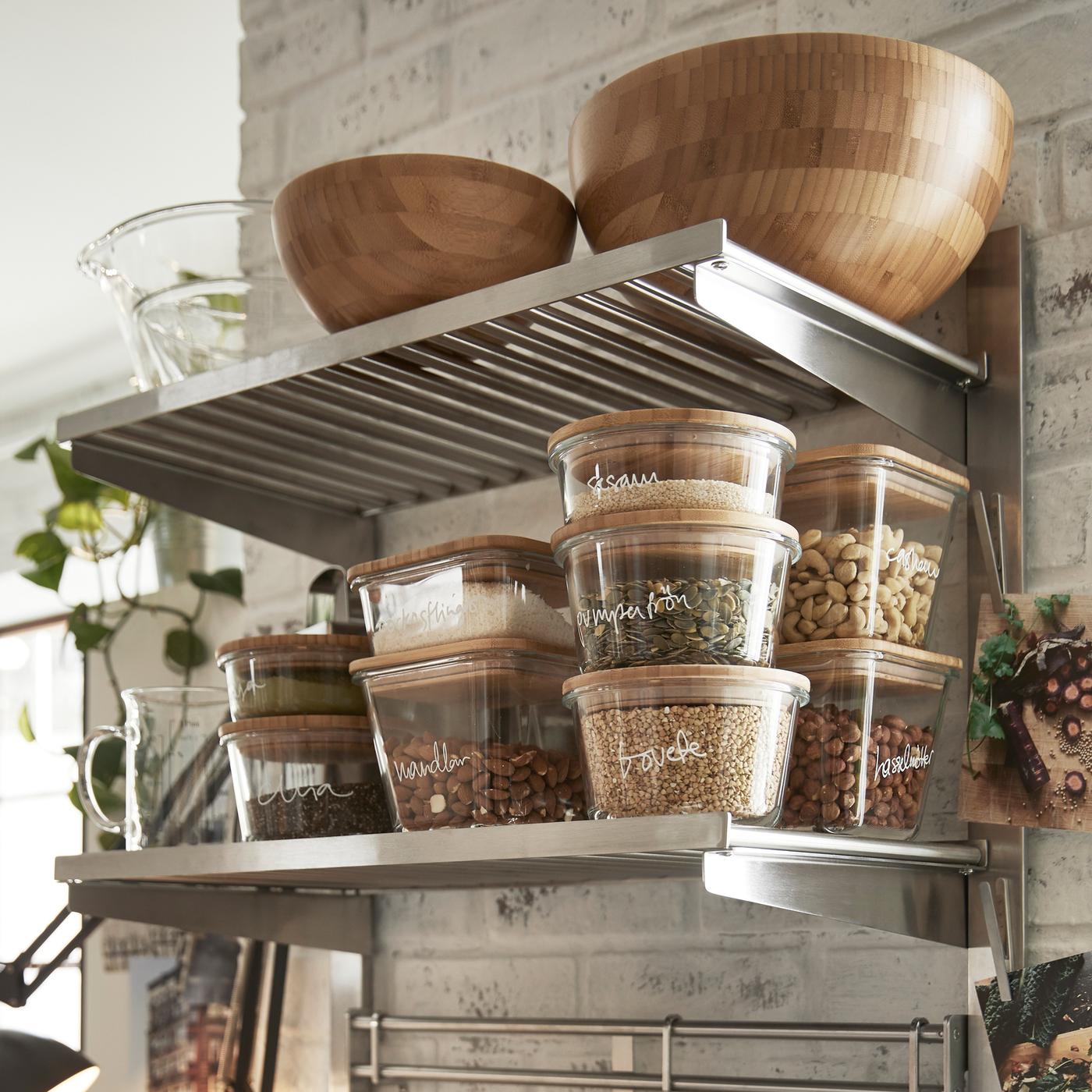 Rail de suspension KUNGSFORS avec tablettes et grilles murales en finition inox/frêne sur lequel sont rangés des plats de service et divers produits alimentaires.