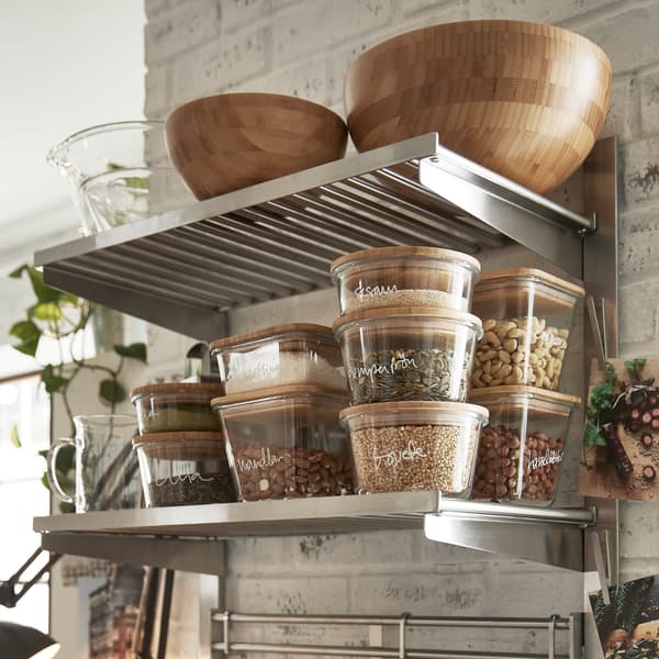Rail de suspension KUNGSFORS avec tablettes et grilles murales en finition inox/frêne sur lequel sont rangés des plats de service et divers articles alimentaires.