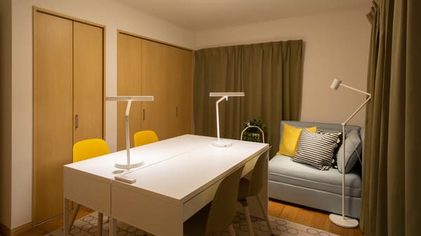 ライトが置かれた白い机が並んでいる。部屋の奥にクッションが置かれたソファがある。