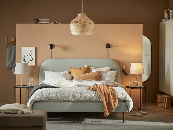 ライトグレーのベッドにベージュの寝具を合わせたシンプル寝室。キャメル色のアクセントで柔らかな雰囲気。
