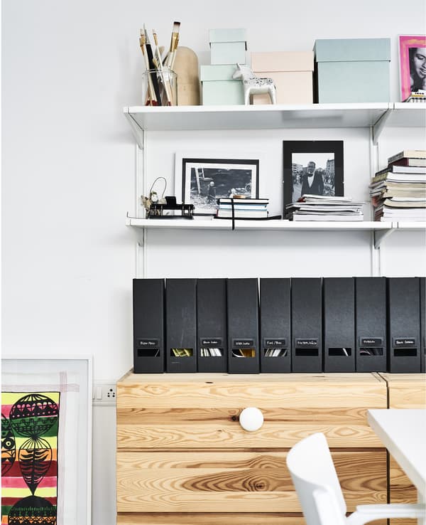Range-revues et tablettes, au-dessus d’une commode en bois.