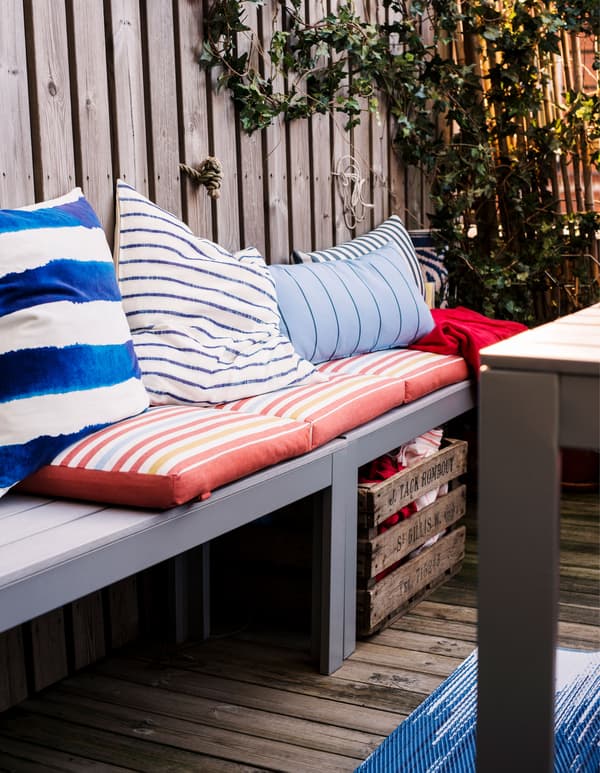 Rangée de bancs en bois avec coussins et bac pour les plaids et les couvertures en dessous.