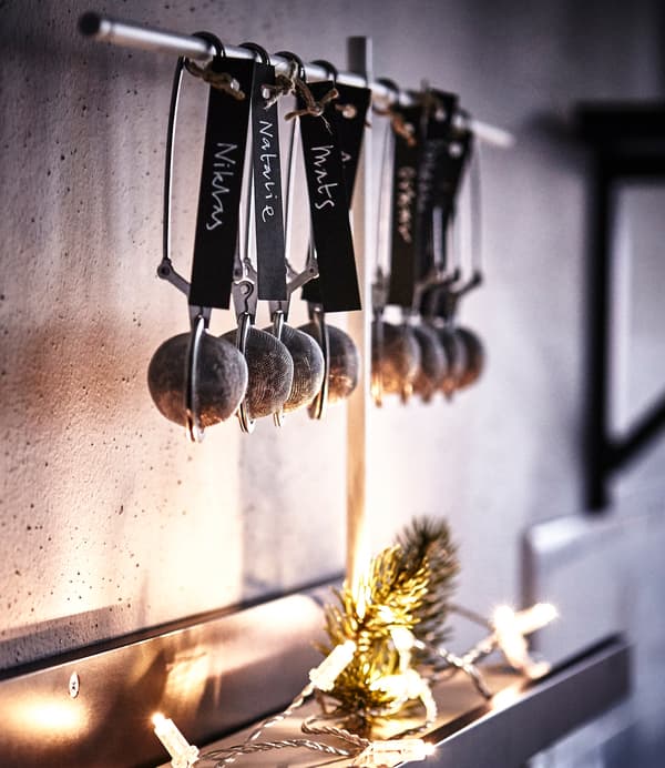 Rangée de boules à thé IKEA IDEALISK accrochées dans une cuisine. Elles contiennent chacune une truffe et portent des étiquettes nominatives.