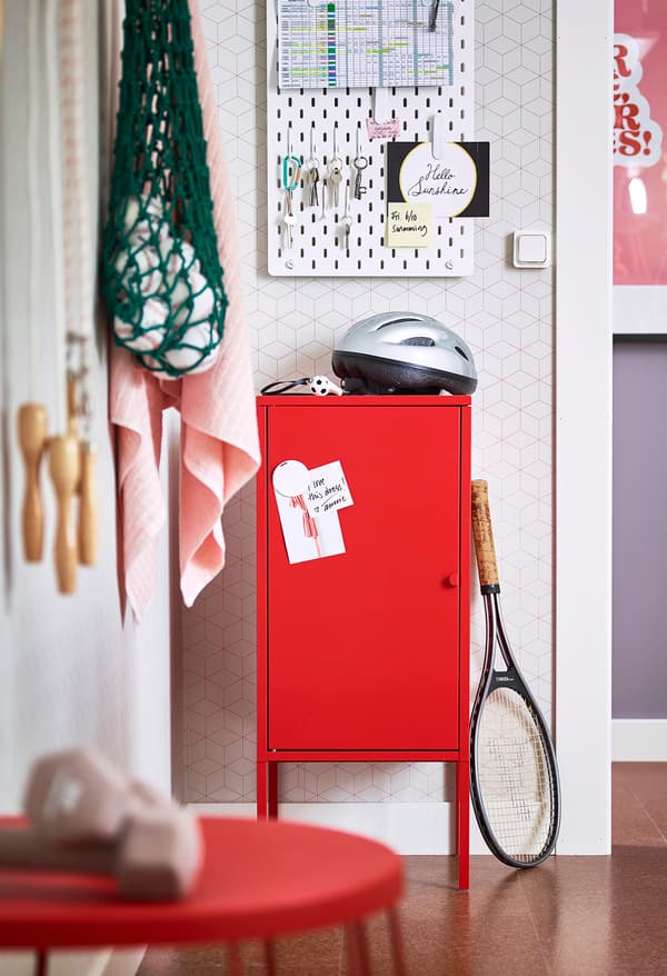Rangement IKEA LIXHULT rouge avec casque de vélo posé dessus et raquette de tennis posée contre