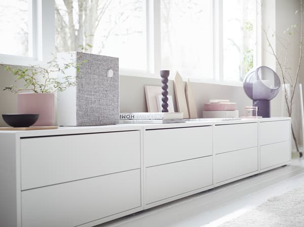 Rangements IKEA EKET en blanc le long d’un appui de fenêtre. Une enceinte Bluetooth ENEBY est posée dessus, ainsi que des livres et des bougeoirs.