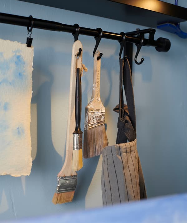 Rangez votre matériel de peinture à portée de main. Suspendez-le à une tringle à rideau, comme la combinaison de tringle à rideau IKEA RÄCKA en noir.