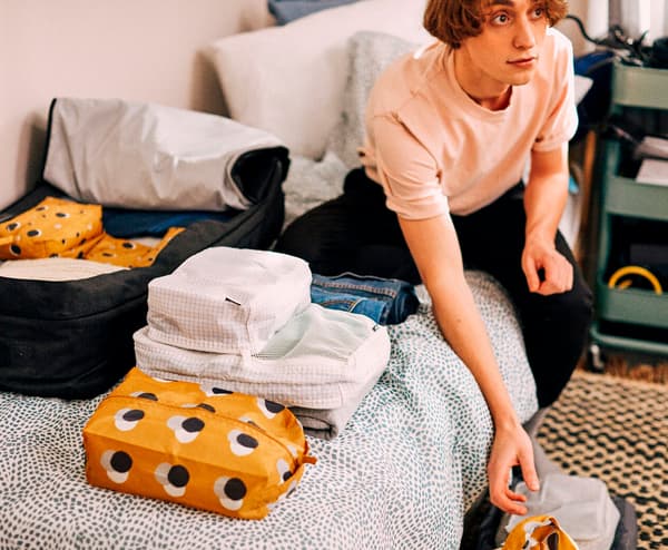 Rapaz novo sentado sobre a súa cama, con todo o que vai meter na maleta para a universidade, organizadas en bolsas RENSARE.