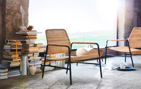 Rattan and metal chairs, and a footstool in front of piles of books and a large window.