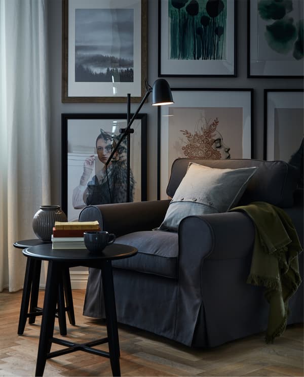 Reading nook with a big, soft armchair, reading light, books on a coffee table and the wall behind covered in art.