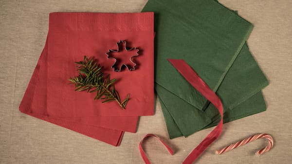 Red and green napkins, a red silk ribbon, a gingerbread man and a spruce branch. All laid out on a tablecloth. 