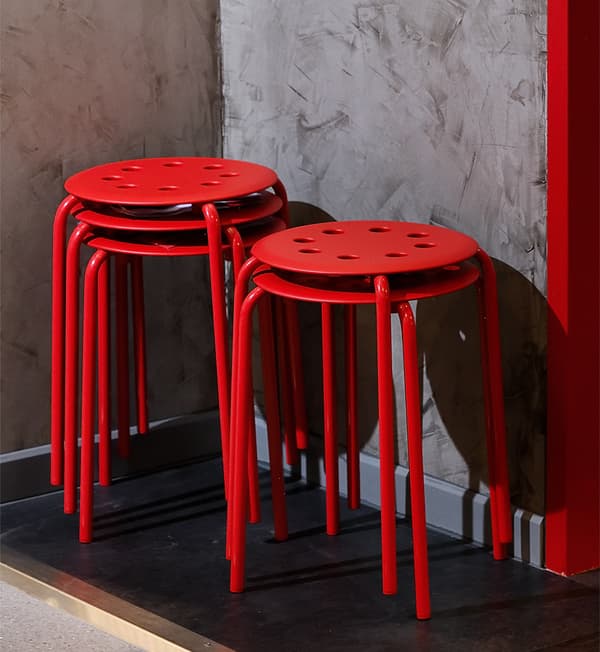 Red chairs are stacked on each other and placed against a grey wall.