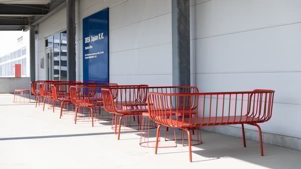 Red metal benches lined up outside a building with a blue sign on the wall.