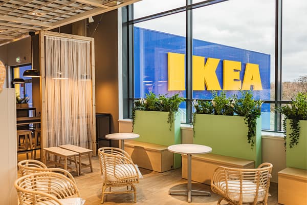 Restauracja w sklepie IKEA Szczecin. Wewnątrz rattanowe fotele, stoliki, donice z zielenią. Dalej okno, przez które widać napis IKEA na elewacji budynku.