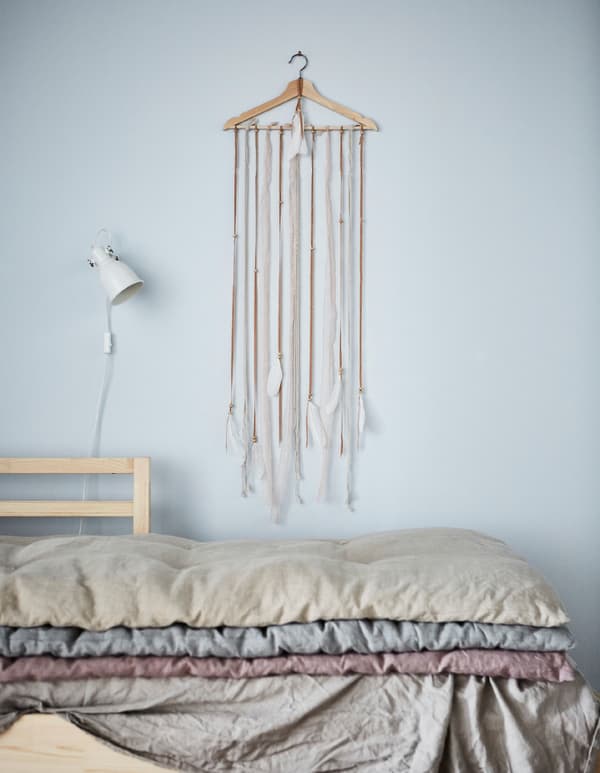 Retallos de tea longos con plumas colgados dunha percha de madeira BUMERANG nunha parede: decoración caseira en estado puro.