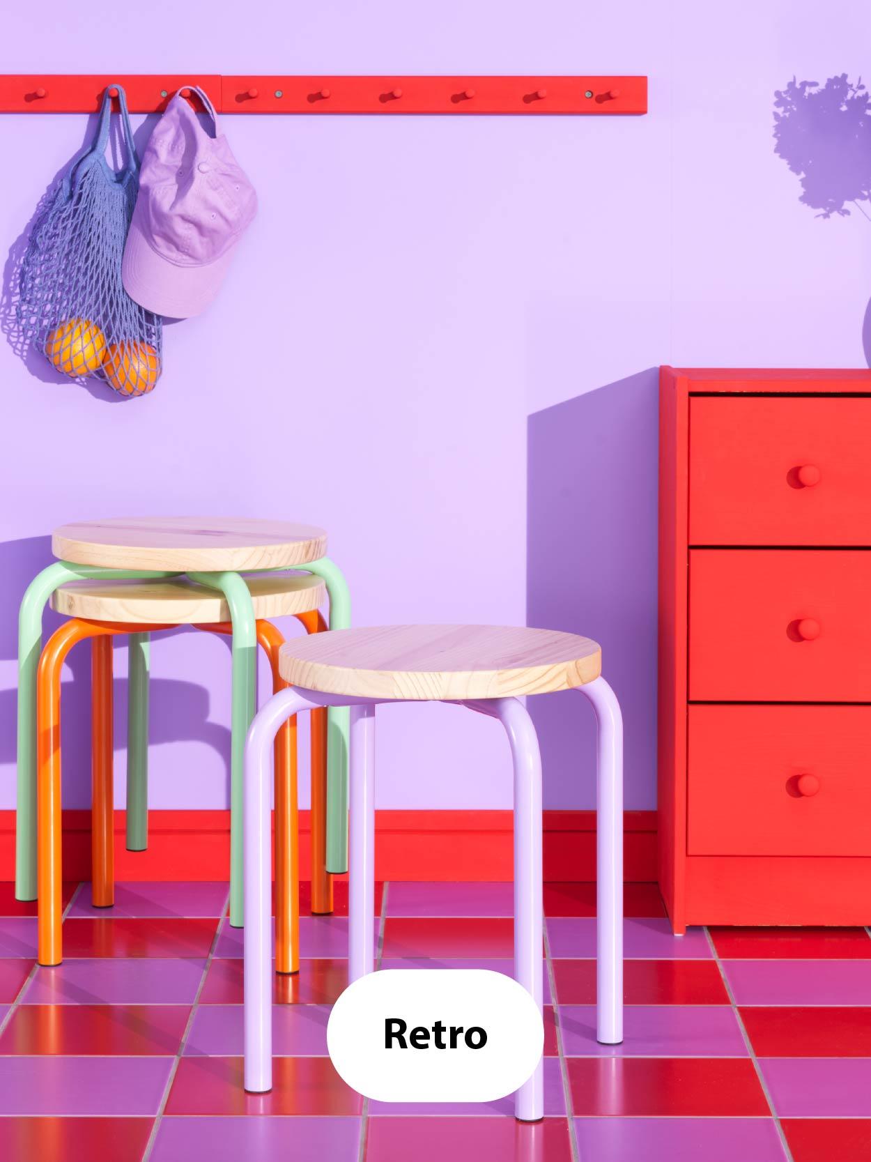 Retro – Playful space with purple walls, red drawer unit, bright red coat rack, and pastel-colored stools on a glossy red-tiled floor.