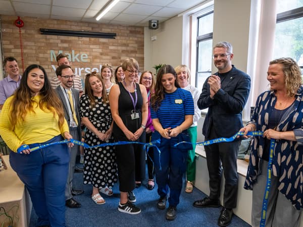 Ribbon cutting to open the space. IKEA co-worker in blue tshirt cutting the ribbon, with a group of people in the background.