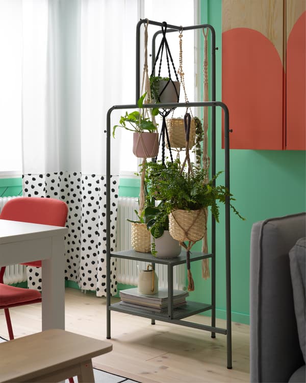 Rideaux blancs à pois noirs et portant gris-vert sur lequel sont suspendues de nombreuses plantes vertes.