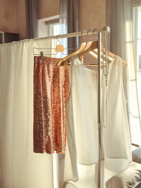 ฉากกั้นห้องทำจากราวแขวนผ้า RIGGA/ริกก้า และผ้าคลุมเตียง VÅRELD/วัวเรลด์ ที่คลุมราวแขวนผ้าไว้และไม้แขวนเสื้อที่แขวนชุดสำหรับงานเลี้ยง