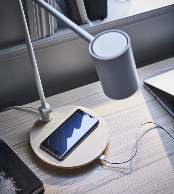 RIGGAD; a work lamp and wireless charger in one, sitting on a desk with a phone charging on it.