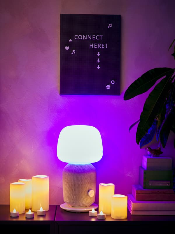 Ripiano con una lampada da tavolo accesa SYMFONISK con cassa Wi-Fi, ceri a LED e candeline, una bacheca SVENSÅS fissata alla parete - IKEA