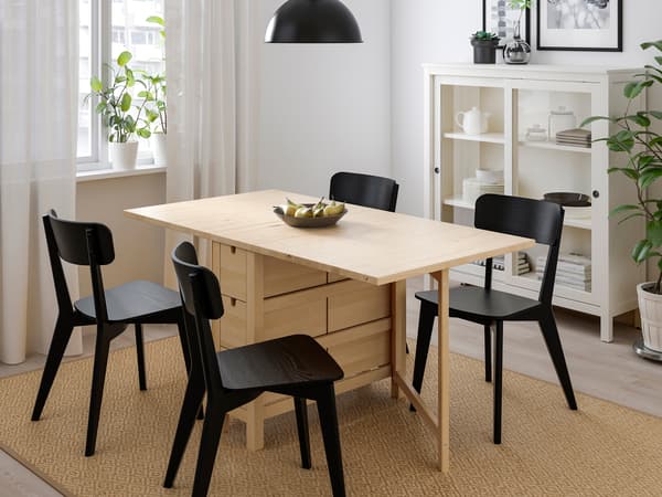 折りたたみ式の木製テーブルと黒い椅子を組み合わせた省スペースダイニング。窓辺で明るい空間。