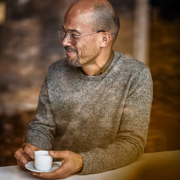رجل في منتصف العمر مبتسم يرتدي نظارات ويستمتع بشرب القهوة