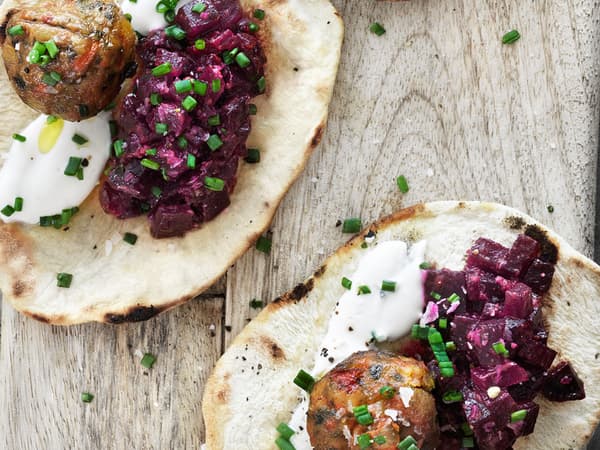 Roasted beet relish and veggie balls on naan bread garnished with yoghurt and chopped chives, served on a wooden board, seen from above.